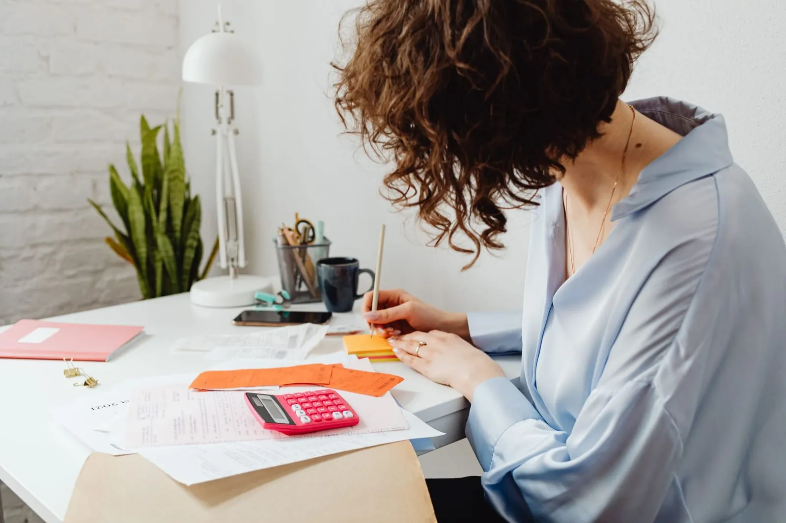 Une personne fait ses comptes à un bureau, calculatrice et factures étalées devant elle.